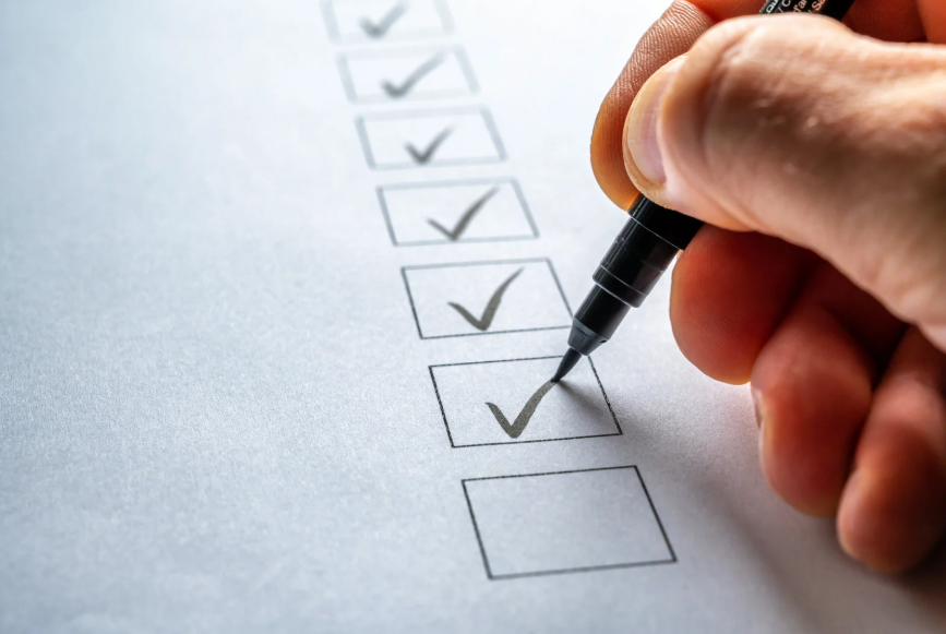 Hand holding a black pen marks a gray check in a row of outlined boxes on white paper, with several completed checks above.