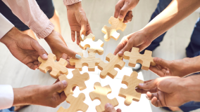 Employees hold puzzle pieces together in a circle.