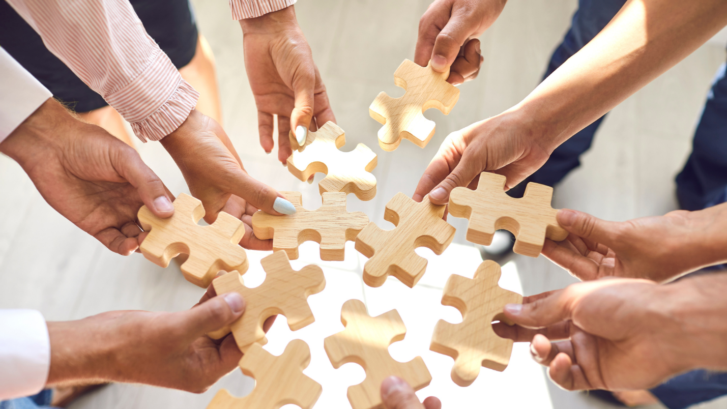 Employees hold puzzle pieces together in a circle.