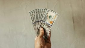 A close up of a person’s hand with a large bundle of cash, indicating financial wealth.