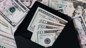 A black envelope filled with twenty dollar bills with many bills in the background.