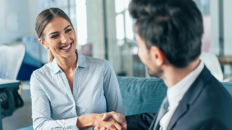 A businesswoman smiles warmly while greeting a businessman.