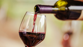 A wine glass being filled with dark red wine from a green bottle.